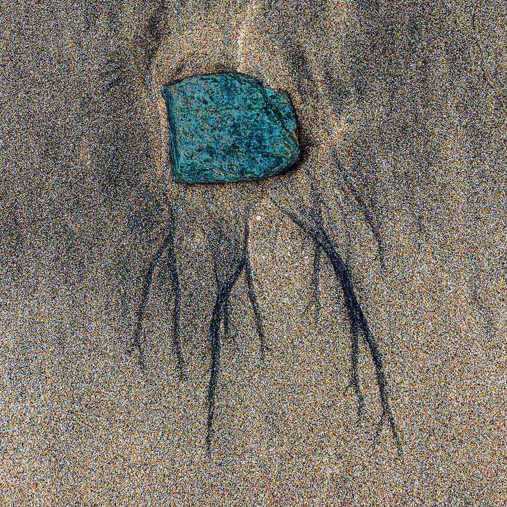 strands | A green blue stone, cupped in a hollow in sand, and shadows on a Breton beachh