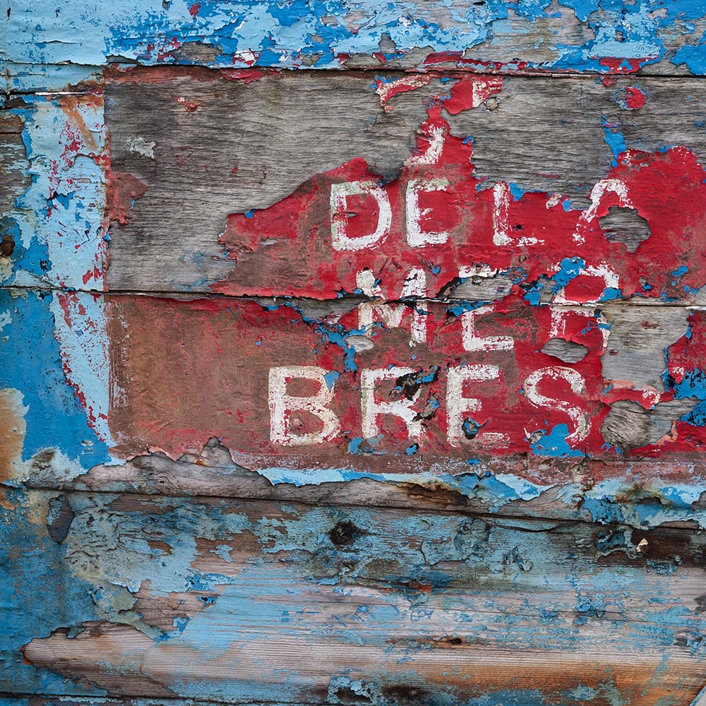 Camaret-sur_mer | a ships name in hand-drawn script on the side of a rotting hulk of a fishing boat