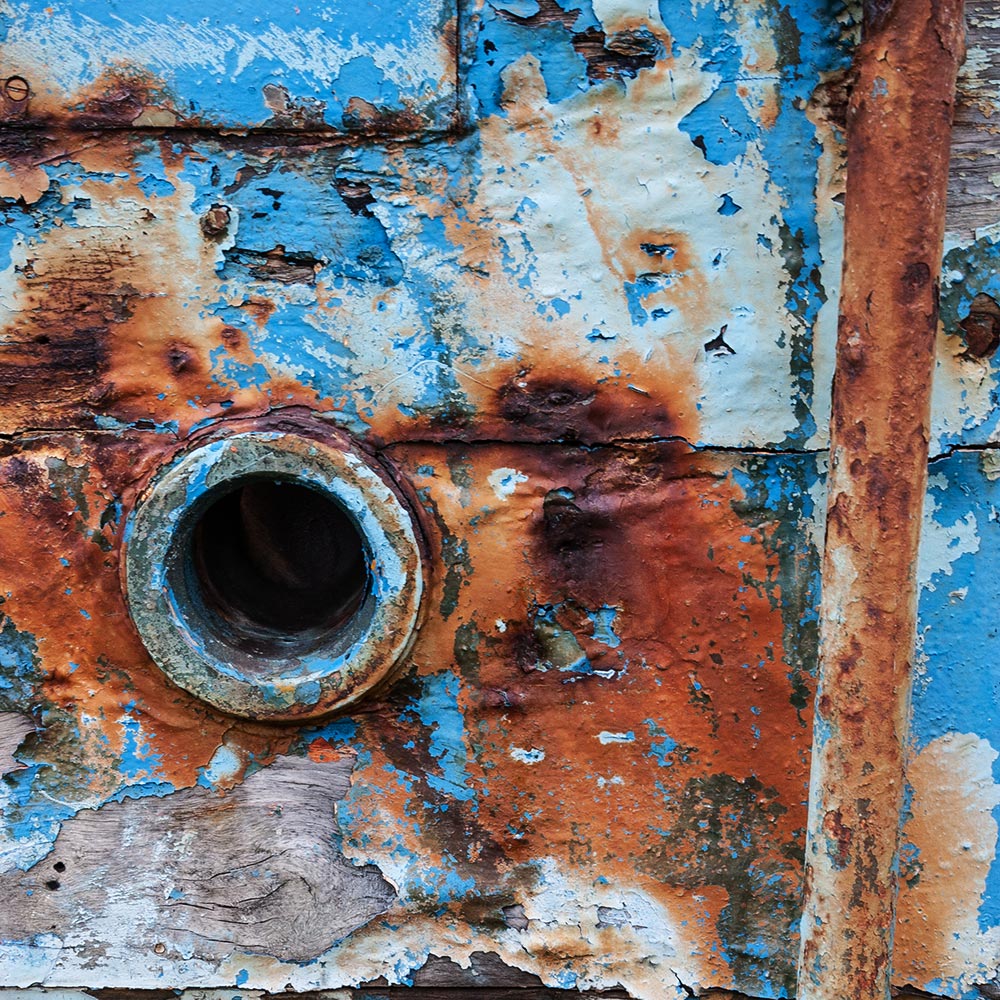 Camaret-sur_mer | a water waste pipe with peeling paint on the side of a rotting hulk of a fishing boat