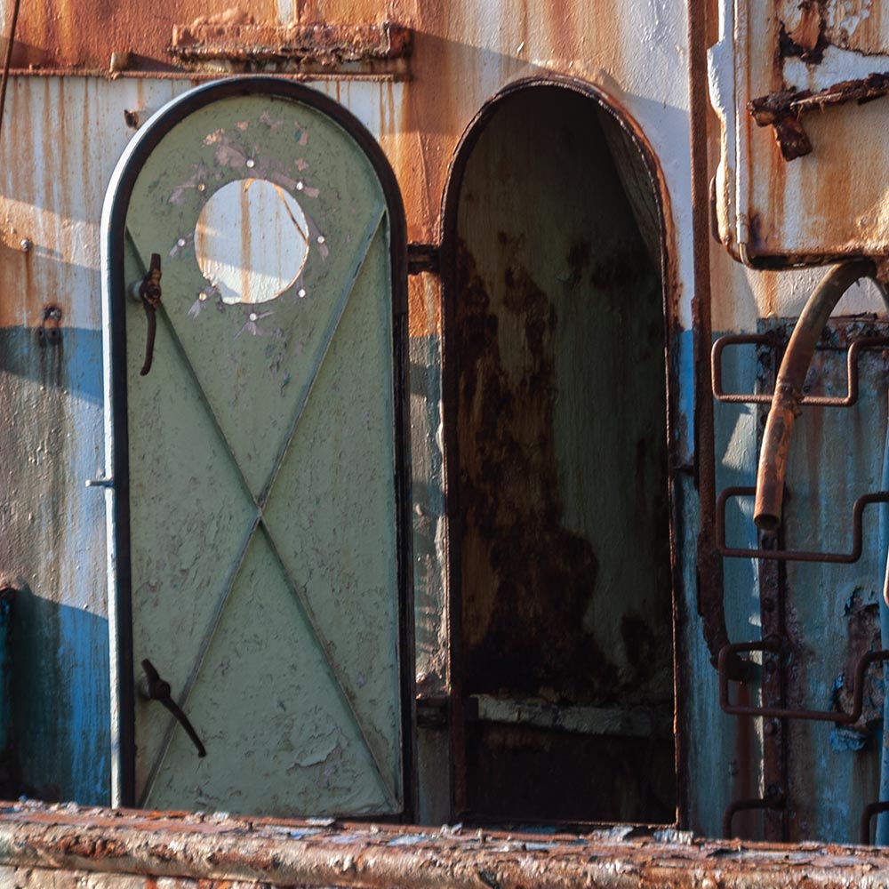 Camaret-sur_mer | a ships open steel door on the rusting superstructure of a rotting hulk of a fishing boat with rust marks on the paint