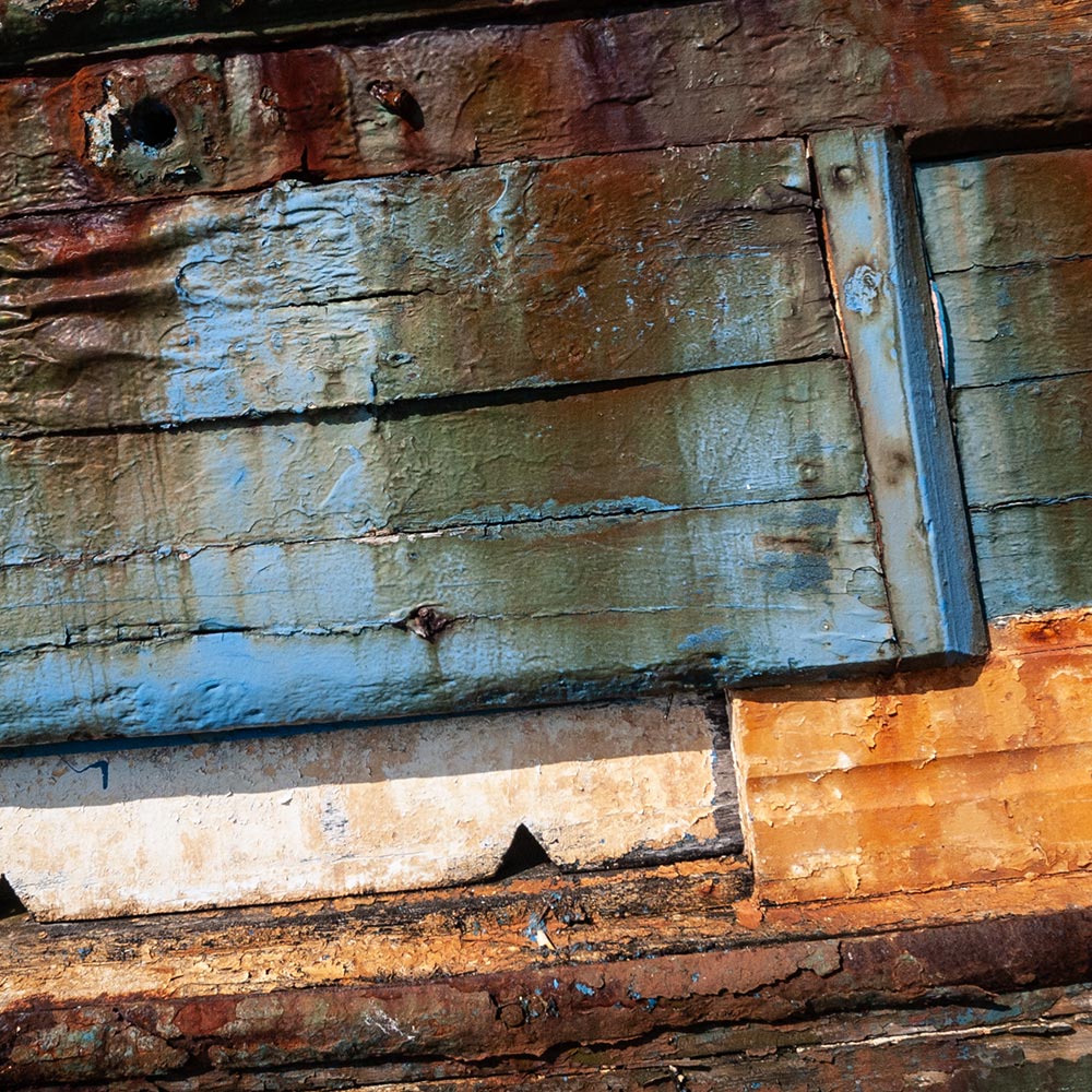 Camaret-sur_mer | The side of a rotting hulk of a fishing boat with peeling rusty blue, yellow and white paint