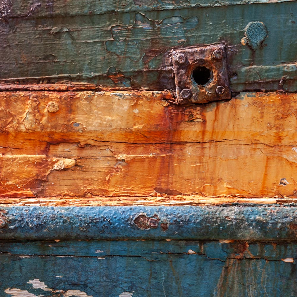 Camaret-sur_mer | a water waste pipe with peeling paint on the side of a rotting blue and yellow hulk of a fishing boat