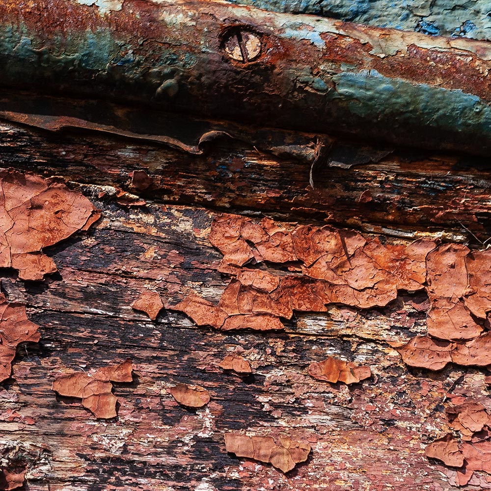 Camaret-sur_mer | Cracked peeling paint side of a rotting hulk of a fishing boat with rusty blue, and raw earth, ochre paint