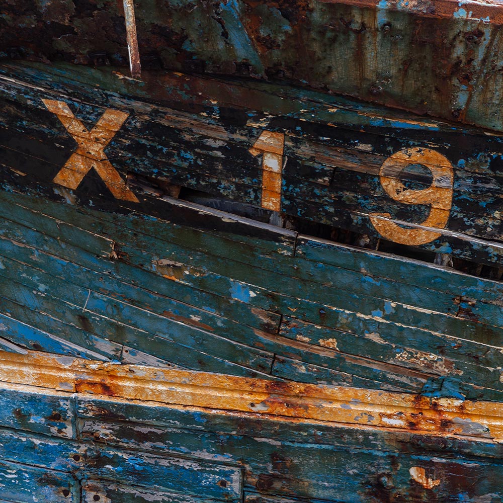 Camaret-sur_mer | The registration number X19 on side of a rotting hulk of a fishing boat with peeling rusty blue, and yellow paint