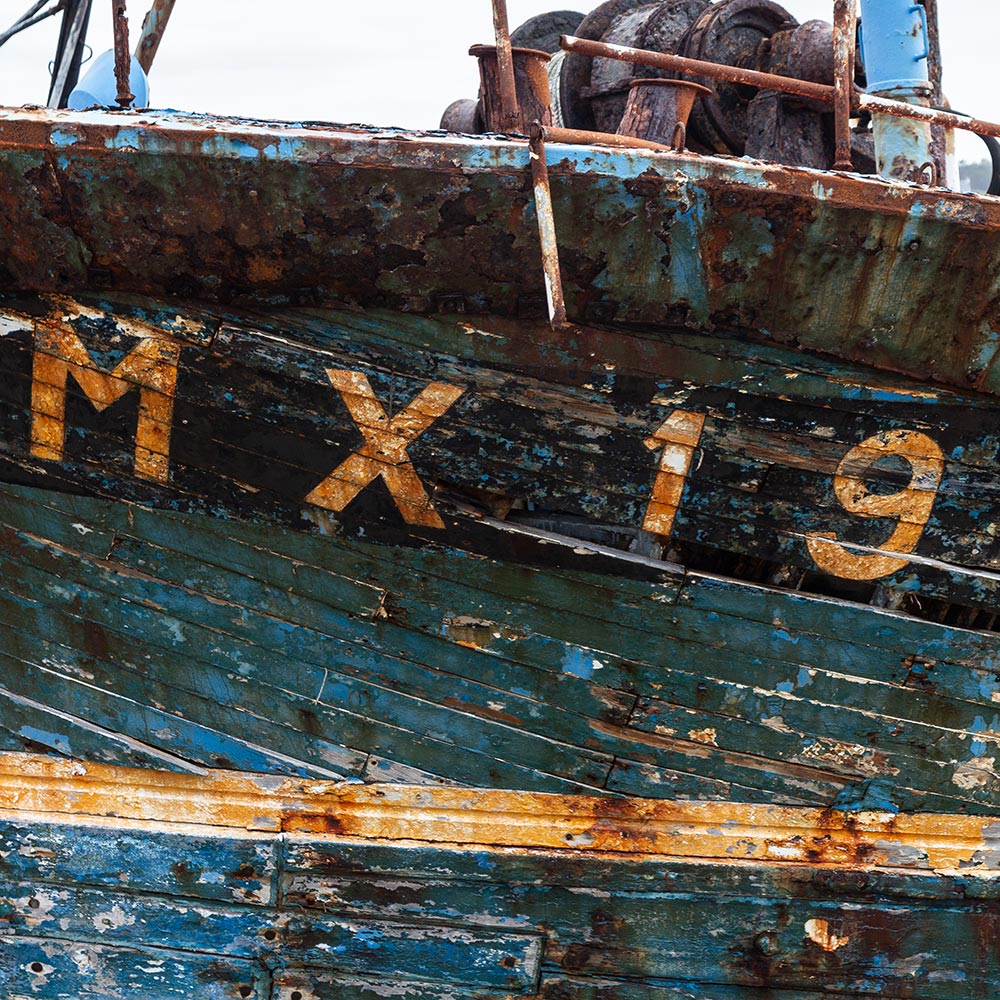 Camaret-sur_mer | The registration number MX19 on side of a rotting hulk of a fishing boat with peeling rusty blue, and yellow paint. Winding gear on deck