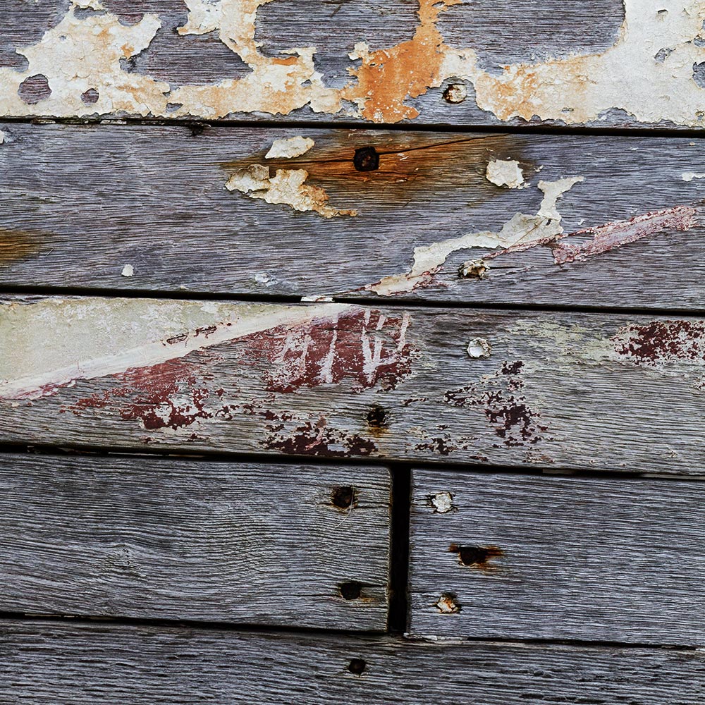 Camaret-sur_mer | The side of a rotting hulk of a fishing boat with peeling rusty white and red paint. Deeply textured worn panks of wood
