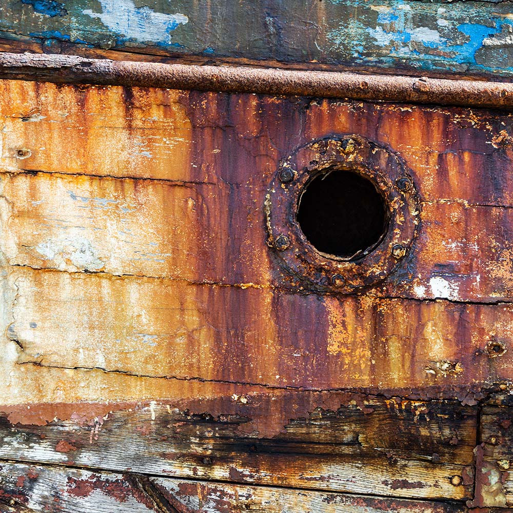 Camaret-sur_mer | a water waste pipe with peeling yellow, blue paint on the side of a rotting hulk of a fishing boat