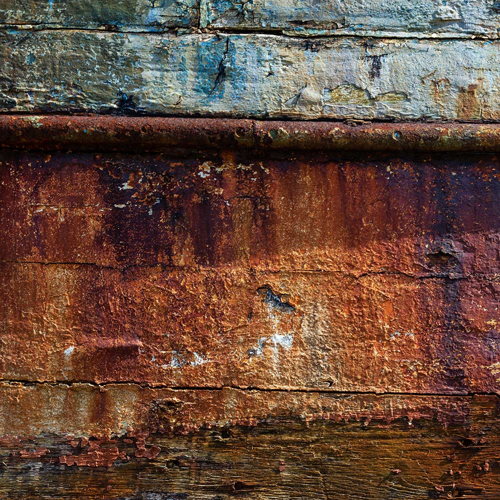 Camaret-sur_mer | Peeling burnt sienna and blue paint and a rusty iron band on the side of a rotting hulk of a fishing boat
