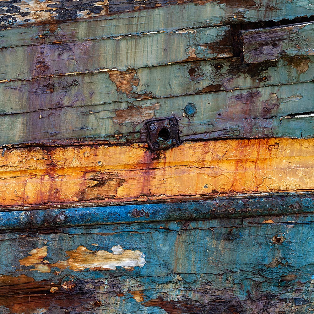 Camaret-sur_mer | The side of a rotting hulk of a fishing boat with peeling rusty green, blue and yellow paint