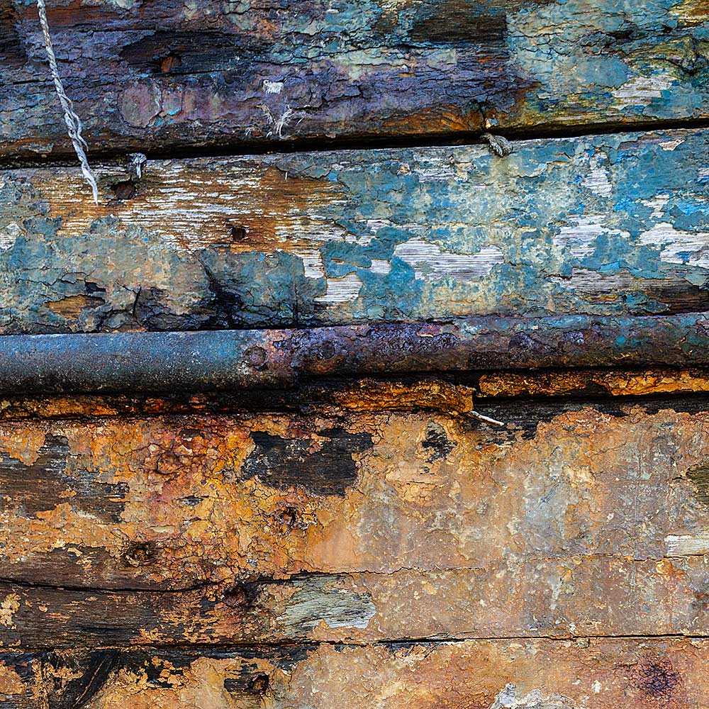 Camaret-sur_mer | The side of a rotting hulk of a fishing boat with peeling rusty green, blue and yellow paint
